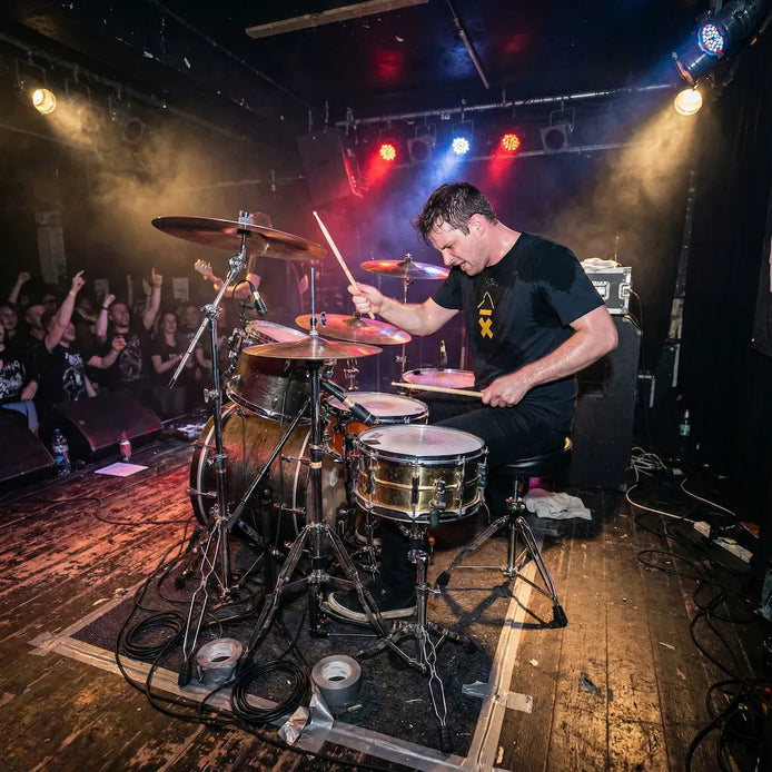 Drummer performing on stage with a band in a dimly lit venue.
