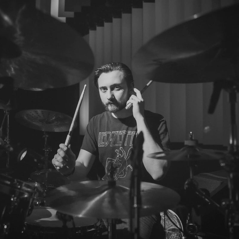 black and white image of Nic Collins, Above Average endorser, sat behind a drum kit, sticks in hand