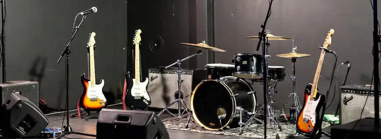 picture of a stage at a small venue ready for a gig. On the stage there are three guitars on stands, microphone stands and a drum kit