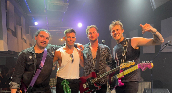 Four musicians from Cancel The Transmission band posing on stage with their instruments