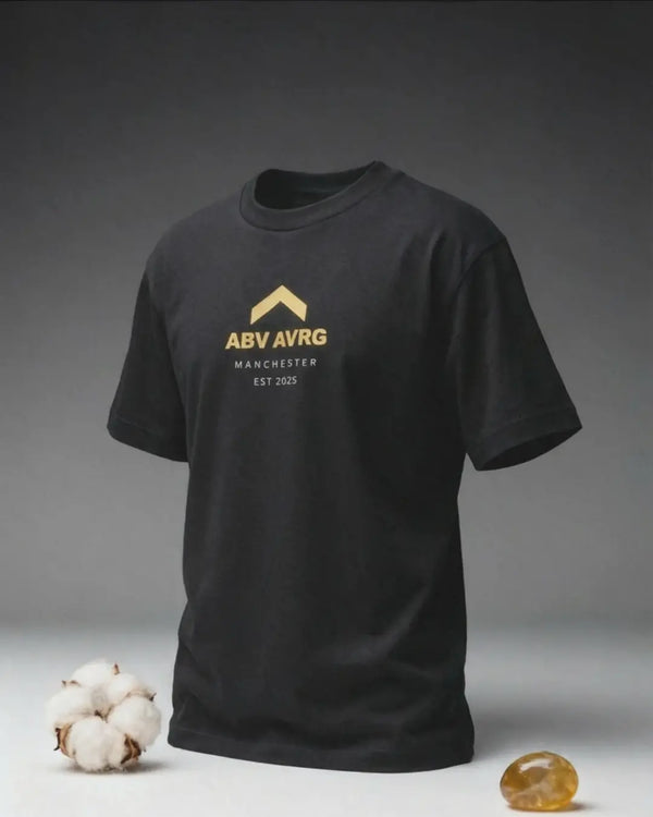 Black CORE organic cotton tee by Above Average Clothing featuring gold ABV AVRG caret logo with Manchester EST 2025 text, sustainable mindset-led streetwear designed in the UK for everyday wear.