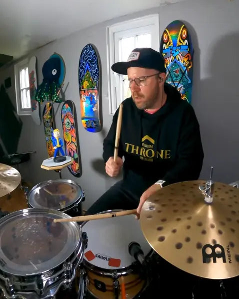 Tom Howarth drumming in his favourite hoodie from Above Average Clothing with the slogan it's called a THRONE for a reason